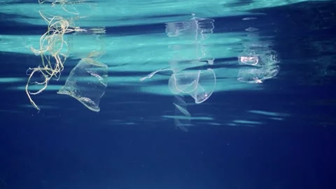 Close up of plastic debris floating below surface in blue water, Slow motion Stock Footage 246359251