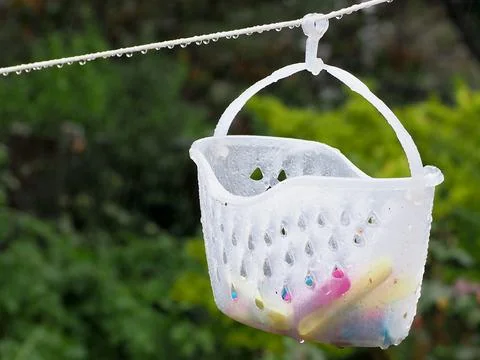 Close up of a plastic peg basket hanging from a washing line with water drops on Stock Photos
