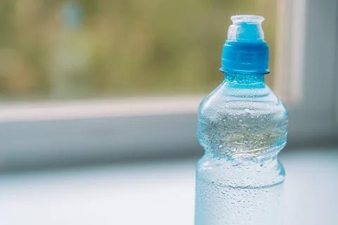 Close-up of plastic water bottle with blue cap near window Stock-Fotos