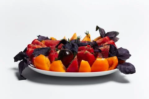 Close-up of plate with mix of different tomatoes with basil leaves, on white. Stock Photos