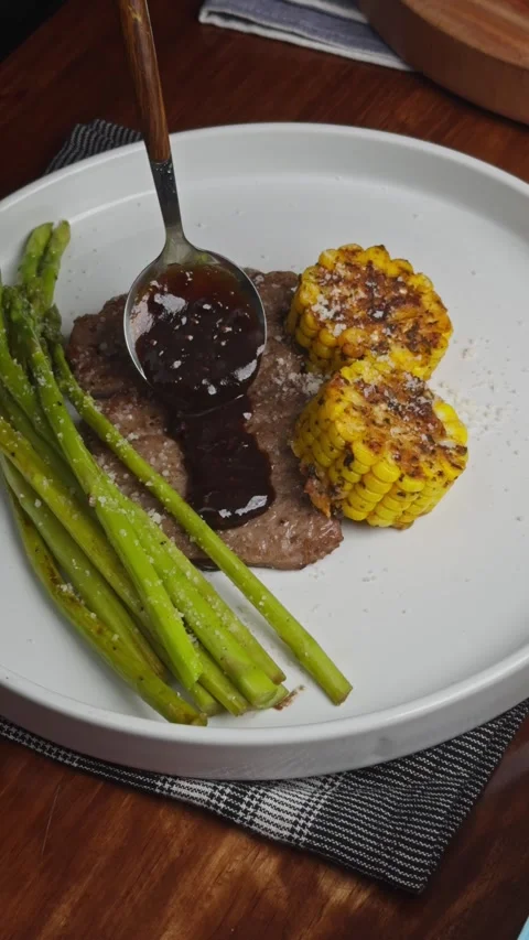 Close up of plated beef steak with grilled corn and asparagus while chef pours Stock Footage 335377222
