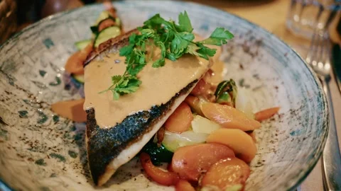 Close up of a plated fish fillet served with vegetables and creamy sauce in a Stock Footage 325727650
