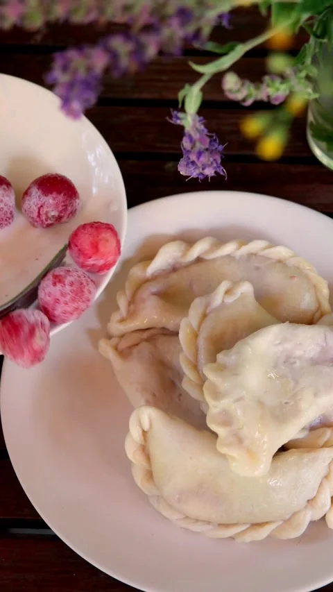 Close-up of plated varenyky dumplings with sugared raspberries on white round Stock Footage 345161812