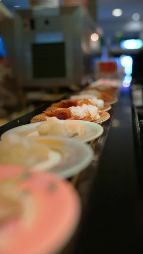 Close up of plates with sushi placed on a rotating conveyor belt moving through Stock Footage 309550604