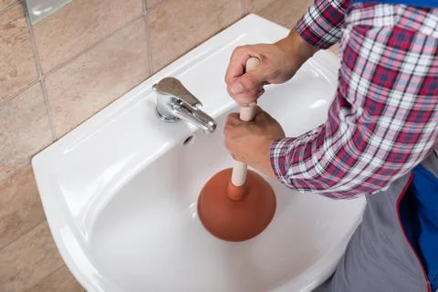 Close-up Of A Plumber Using Plunger In Bathroom Sink Stock Photos