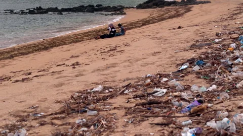 Close polluted beach with plastic trash foreground and people near surf 動画素材 340140722