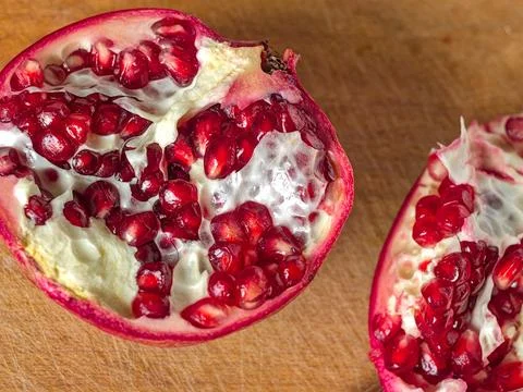 Close-up of Pomegranate Half Showing Ruby Red Arils and White Pith on a Wooden C Foto stock