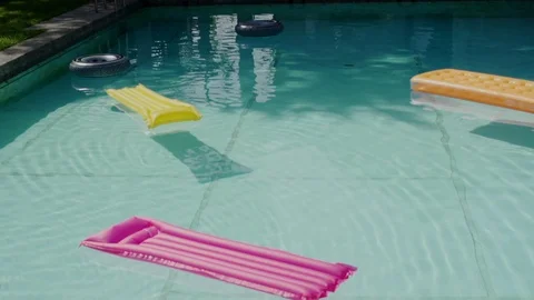 Close up of pool with inflatable rubber loungers on water surface in slow motion Stock Footage 128965467