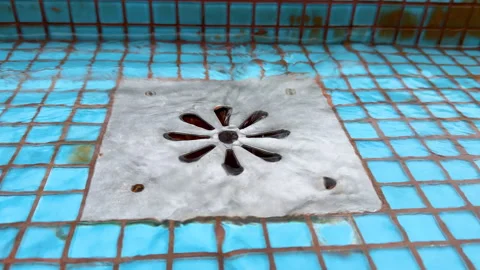 Close-up of pool water pouring into metallic floor drain in a blue tiled pool Stock Footage 293075256