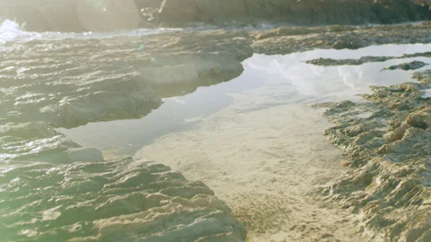 Close up of pool of water with reflections of sunlight as ocean waves crash on r Stock Footage 199457525
