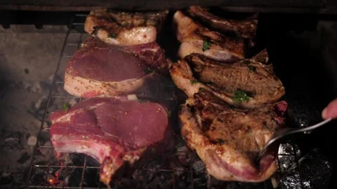 A close-up of a pork steak being grilled on hot coals, a man turns the meat. Stock Footage 295843854