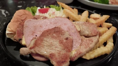 Close-up of a pork steak topped with ham and served with crispy French fries Stock Footage 343552252