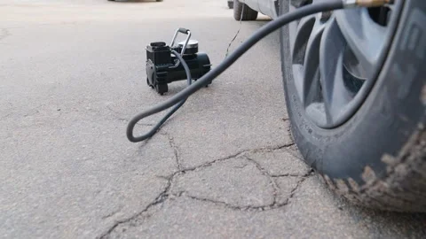 Close-up of a portable electric air compressor inflating a car tire on a cracked Stock Footage 329285034