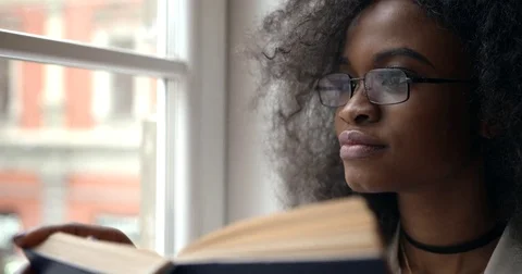 Close-up portrait of the 20-year old afro-american woman in glasses reading the Stock Footage 83368939