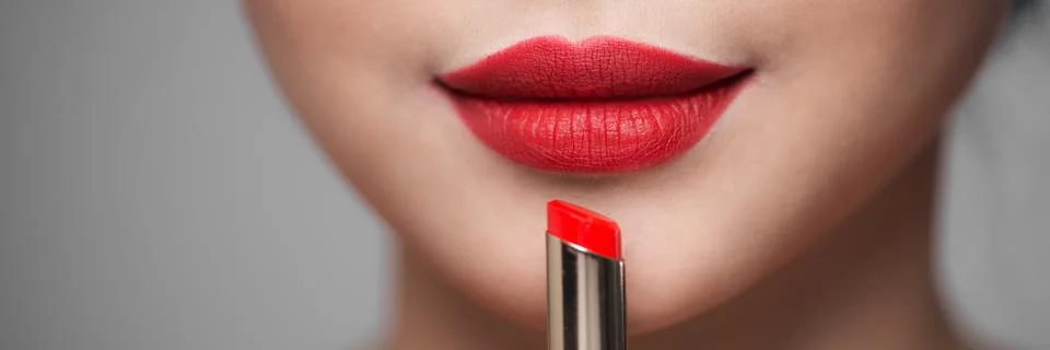 Close up portrait of attractive girl rouging her lips. She is holding red lip Stock Photos