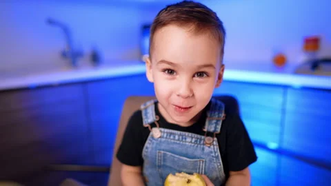 Close portrait of boy biting yellow apple with both hands. A child wears denim Stock Footage 343381249