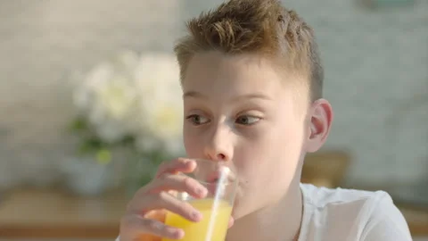Close up portrait of boy drinking fresh orange juice for breakfast Stock Footage 196706077