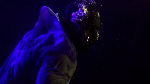 Close-up portrait of a dark-skinned man who is under water. It floats on a dark 스톡 동영상 134737068