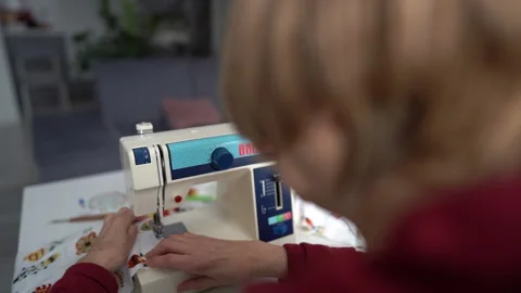 Close up portrait of an elderly seamstress. Back view. Pensioner sews curtains Stock Footage 148493293