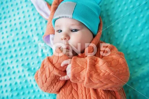 A close-up portrait of a funny baby wearing a hat and a jumsuit of a hare. Fa Stock Photos