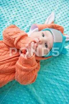 A close-up portrait of a funny baby wearing a hat and a jumsuit of a hare. Fa Stock Photos
