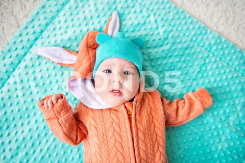 A close-up portrait of a funny baby wearing a hat and a jumsuit of a hare. Fa Stock Photos