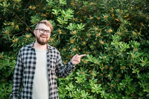 Close up portrait handsome young man point over green bush outside copy space Stock Photos