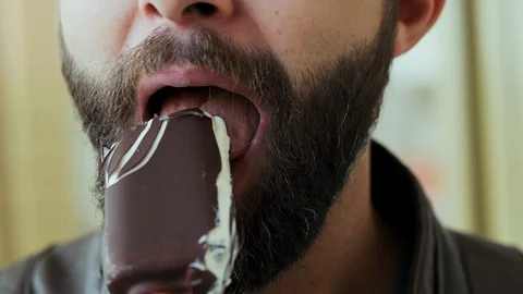 Close-up portrait of hungry bearded man eating chocolate ice cream lolly Stock Footage 107987558