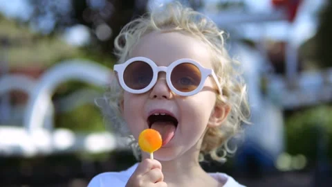 Close up portrait of kid eats caramel sweet sugary lollipop in nature park. Cute Stock Footage 240112200