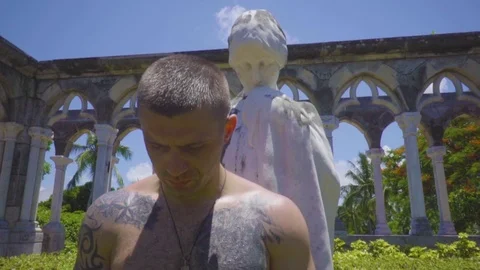 Close up portrait of man stands in front of a statue among ancient columns with Stock Footage 112698173