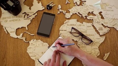 A close portrait of a man writes a plan for his journey. Wooden world map layout Stock Footage 92919675
