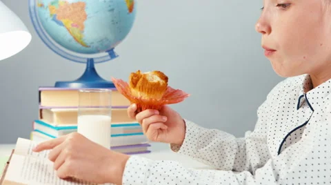 Close up portrait school girl 7-8 years reading book and eating muffin Stock Footage