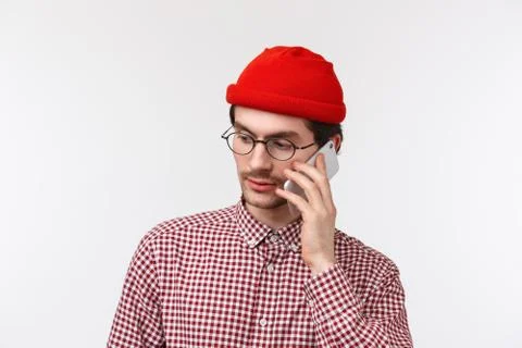Close-up portrait of serious-looking young man in red beanie and glasses calling Stock Photos
