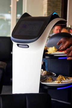 A close portrait of a serving robot on wheels with a screen displaying a cute Stock Photos