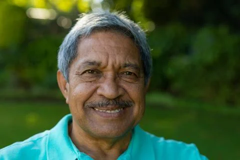 Close-up portrait of smiling biracial senior man with gray hair against plants Stock Photos