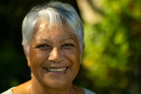 Close-up portrait of smiling biracial senior woman with short gray hair in park Stock Photos