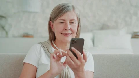 Close up portrait smiling elder middle age woman using smartphone sitting on Vídeos de archivo 224534771
