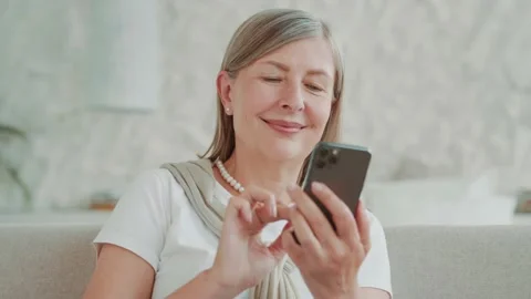 Close up portrait smiling elder middle age woman using smartphone sitting on Vídeos de archivo 224538102