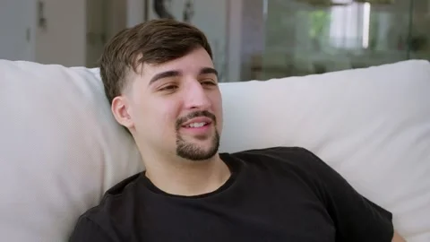 Close-up portrait of smiling man is resting while sitting on couch at home. Stock Footage 247660798