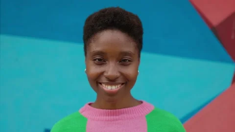 Close up portrait of smiling young black woman against colored wall outdoors Stock Footage 220597947