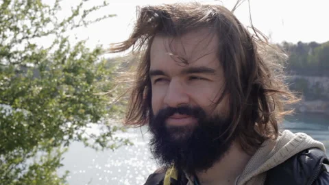 Close-up portrait of a smiling young man with a beard and long brunette hair. Video stock 112641640
