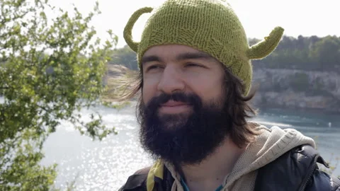Close-up portrait of a smiling young man with a black beard in a knitted hat. Video stock 113791174