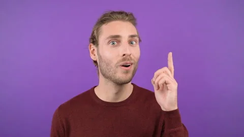 Close-up portrait of surprised young man in burgundy sweater pointing to space Stock Footage 144927376