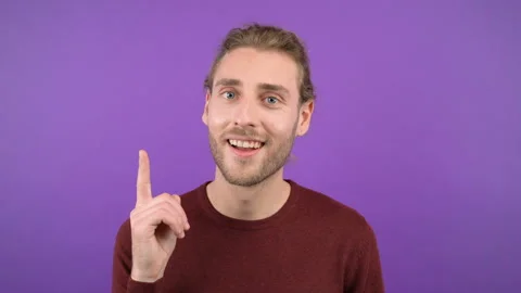 Close-up portrait of surprised young man in burgundy sweater pointing to space Stock Footage 144981670