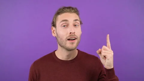Close-up portrait of surprised young man in burgundy sweater pointing to space Stock Footage 145367544