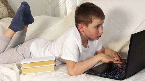 Close up portrait of tired schoolboy lying on sofa and typing text on laptop Stock Footage 154235045