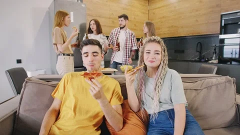 Close-up portrait of two friends, guy and girl, sitting on the sofa with pizza Stock Footage 278487893