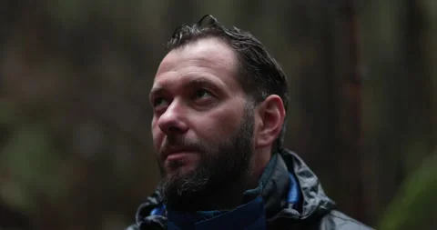 Close-up portrait of a young bearded man sitting in nature between forest Vídeos de archivo 244144336