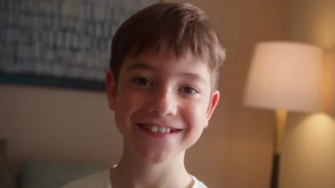 Close up portrait of a young boy smiling and looking at the camera in a cozy Видео 345119559