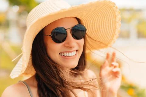 Close up portrait of a young cheerful woman wearing sunglasses and a sunhat. Stock Photos